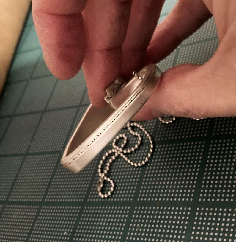May include: A silver bracelet with a decorative design and a chain attached.