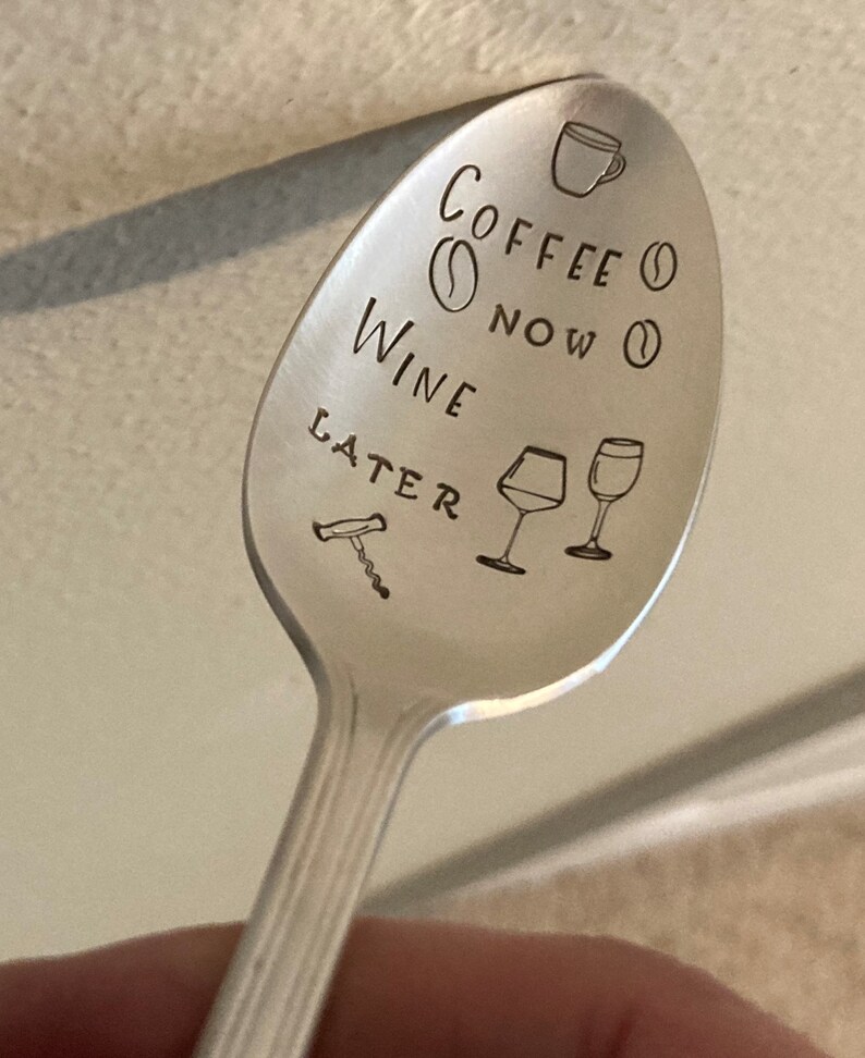 May include: A silver spoon with the text "Coffee Now Wine Later" engraved on it. The spoon also has a coffee cup, coffee bean, wine glass, and corkscrew engraved on it.