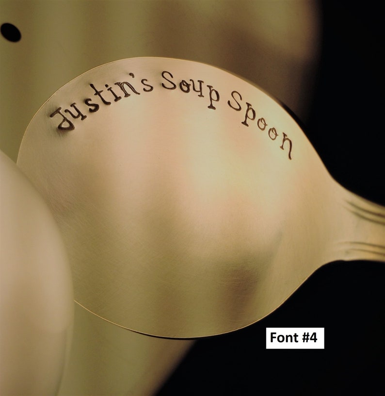 May include: A gold-colored soup spoon with the words "Justin's Soup Spoon" engraved on the front. The spoon is shown against a light brown background. Font #4.