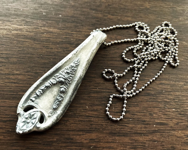 May include: A silver spoon pendant necklace with an ornate design. The spoon is attached to a silver ball chain.