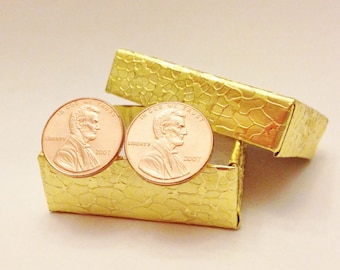 May include: A pair of gold-colored cufflinks in the shape of a 2007 US penny. The cufflinks are in a small, gold-colored box.