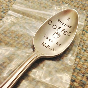 Pu&ograve; includere: Un cucchiaio d'argento con la scritta incisa "I Turned Coffee Into An M.B.A.". Una piccola tazza di caff&egrave; &egrave; incisa tra le parole "Coffee" e "Into". Il cucchiaio &egrave; in un sacchetto di plastica trasparente.