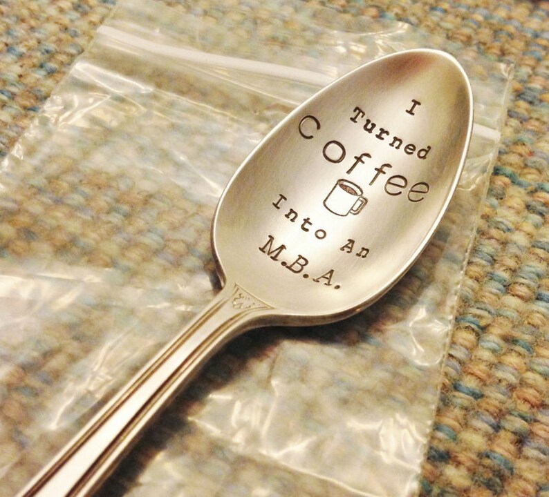 Pu&ograve; includere: Un cucchiaio d'argento con la scritta incisa "I Turned Coffee Into An M.B.A.". Una piccola tazza di caff&egrave; &egrave; incisa tra le parole "Coffee" e "Into". Il cucchiaio &egrave; in un sacchetto di plastica trasparente.