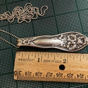 May include: A silver necklace with a floral design. The pendant is a vintage silverware spoon with a floral pattern. The necklace is 2 inches long.