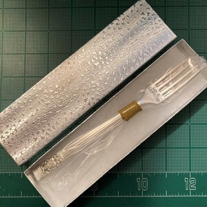 May include: A silver fork with a gold handle in a silver and white box. The fork has the words "30 & LA BELLE" engraved on the handle.