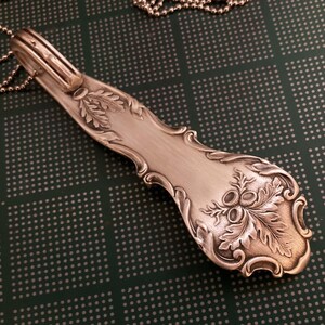 May include: A silver spoon necklace with an acorn design. The spoon is attached to a silver chain.