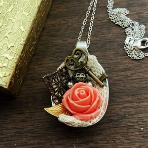 May include: A silver spoon necklace with a coral rose, a key, and lace accents.