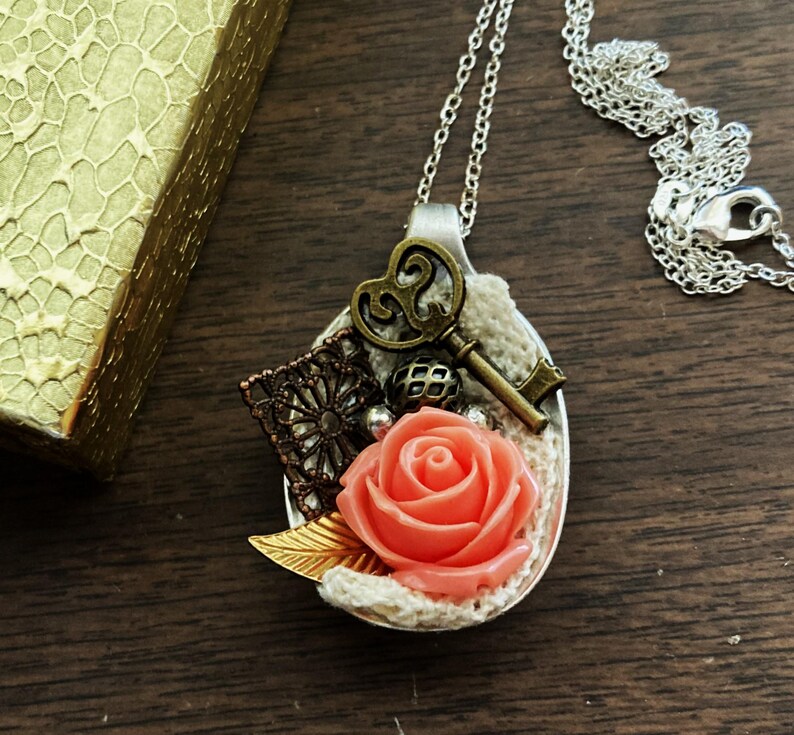 May include: A silver spoon necklace with a coral rose, a key, and lace accents.