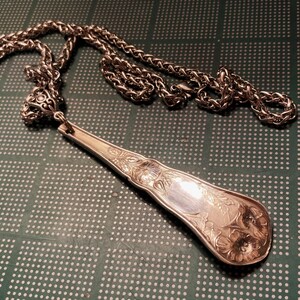 May include: A silver necklace with a detailed, ornate pendant made from a vintage spoon. The pendant has a floral design and is attached to a silver chain.
