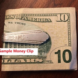 May include: A silver money clip made from a spoon, holding a ten-dollar bill. The money clip has a floral design. The text "Sample Money Clip" is in a white box at the bottom of the image.