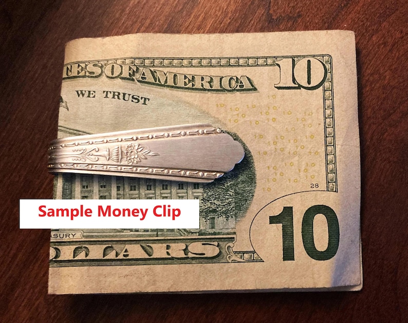 May include: A silver money clip made from a spoon, holding a ten-dollar bill. The money clip has a floral design. The text "Sample Money Clip" is in a white box at the bottom of the image.