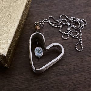 May include: A silver heart-shaped pendant necklace with a pearl-like bead inside. The necklace is on a silver chain.