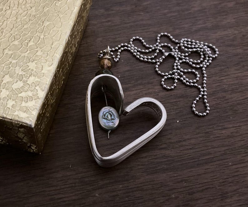 May include: A silver heart-shaped pendant necklace with a pearl-like bead inside. The necklace is on a silver chain.