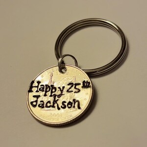 May include: A silver keychain with a quarter coin pendant. The coin is engraved with "Happy 25th Jackson" and the year 2001. The keychain has a split ring for attaching keys.