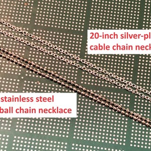 May include: Two silver chains on a green background. The top chain is a 20-inch silver-plated cable chain necklace. The bottom chain is a 20-inch stainless steel 1.5mm ball chain necklace.