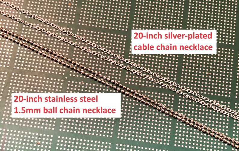 May include: Two silver chains on a green background. The top chain is a 20-inch silver-plated cable chain necklace. The bottom chain is a 20-inch stainless steel 1.5mm ball chain necklace.