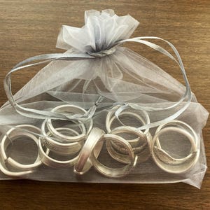 Puede incluir: Una colecci&oacute;n de anillos de servilleta de plata en una bolsa de tul blanca. Los anillos est&aacute;n apilados y superpuestos, creando una exhibici&oacute;n decorativa.