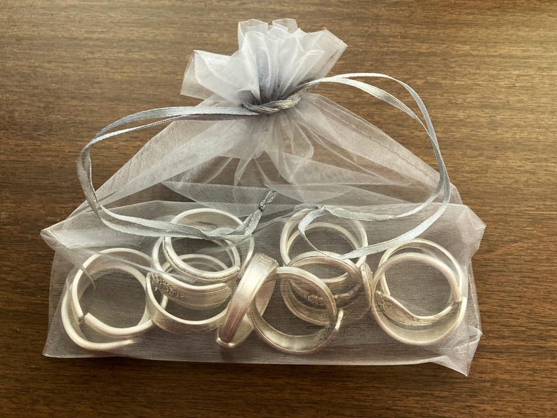 Puede incluir: Una colecci&oacute;n de anillos de servilleta de plata en una bolsa de tul blanca. Los anillos est&aacute;n apilados y superpuestos, creando una exhibici&oacute;n decorativa.
