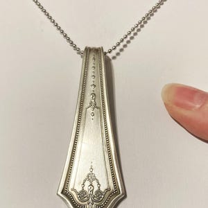 May include: A silver spoon pendant necklace with a decorative design on the handle. The necklace is on a silver chain.