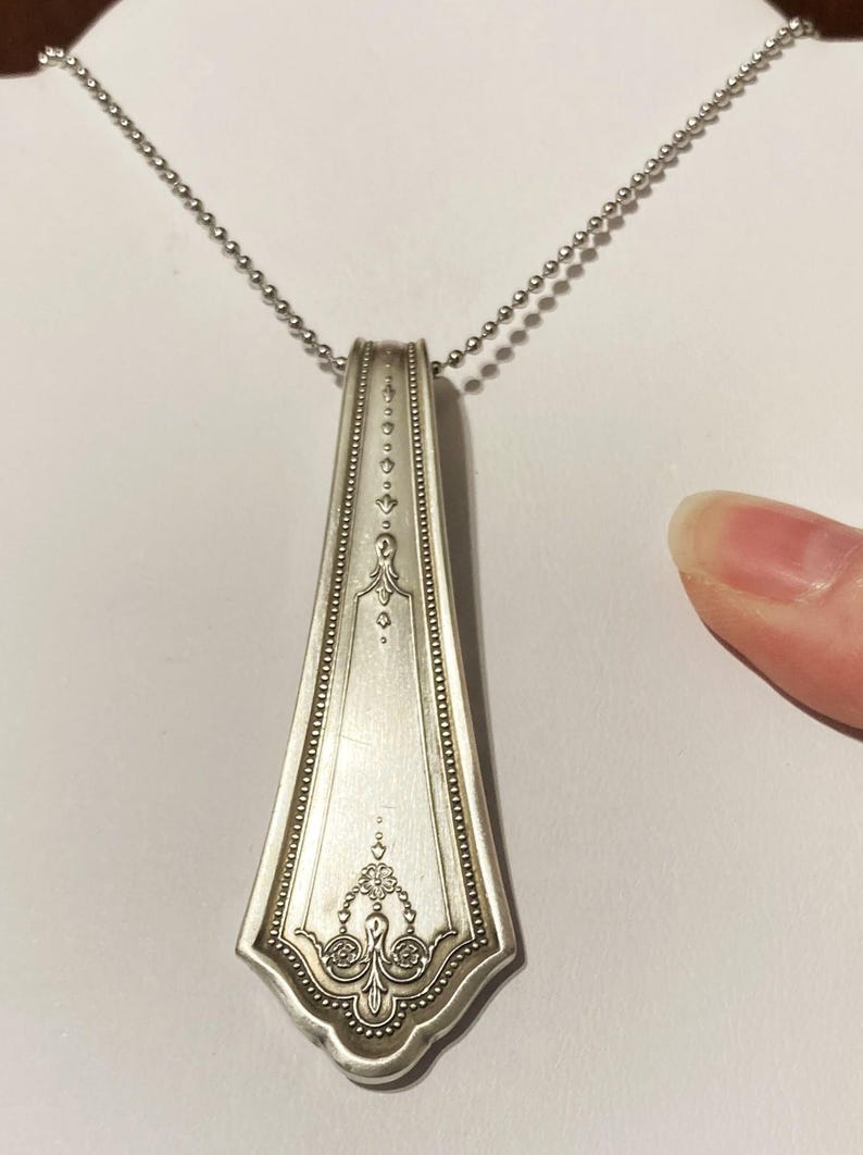 May include: A silver spoon pendant necklace with a decorative design on the handle. The necklace is on a silver chain.
