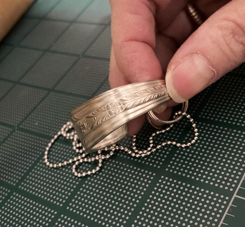 May include: A silver bracelet with an engraved floral design and a silver chain attached.
