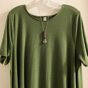 May include: A green short-sleeved t-shirt with a silver necklace featuring a pendant shaped like a stylized human figure.