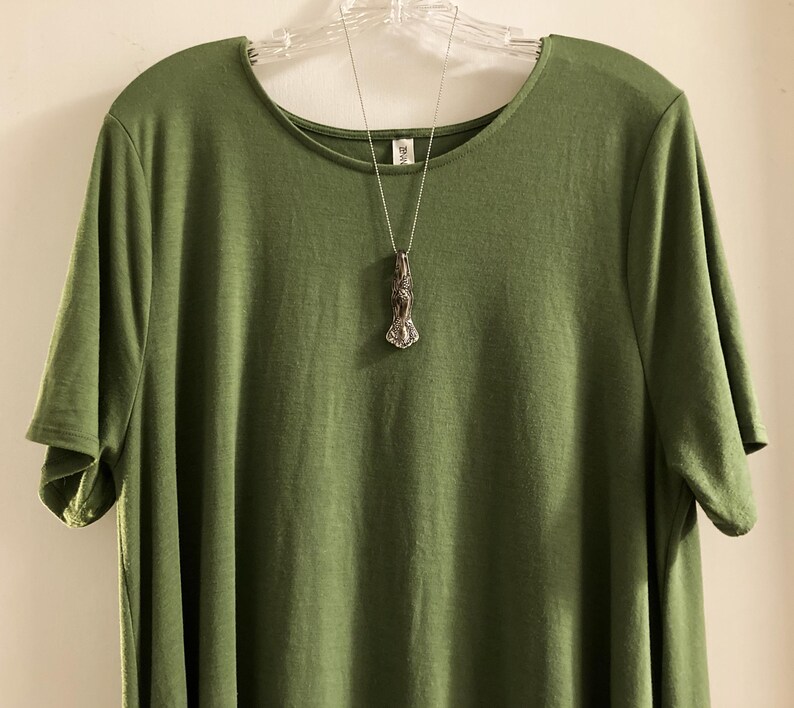 May include: A green short-sleeved t-shirt with a silver necklace featuring a pendant shaped like a stylized human figure.