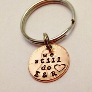 May include: A copper penny keychain with the words "We still do" and a heart with the year 2017 engraved on it. The keychain is attached to a silver key ring.