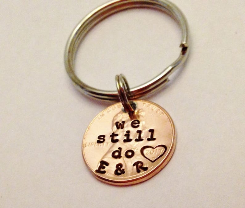 May include: A copper penny keychain with the words "We still do" and a heart with the year 2017 engraved on it. The keychain is attached to a silver key ring.