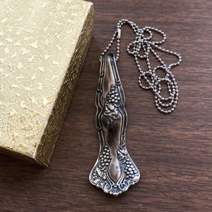May include: A silver necklace with a pendant made from a vintage silverware piece featuring a grapevine design. The pendant is attached to a silver ball chain.