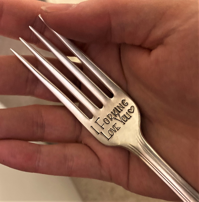 Op de afbeelding: Een zilveren vork met de woorden "I forking love you" gegraveerd op het handvat.