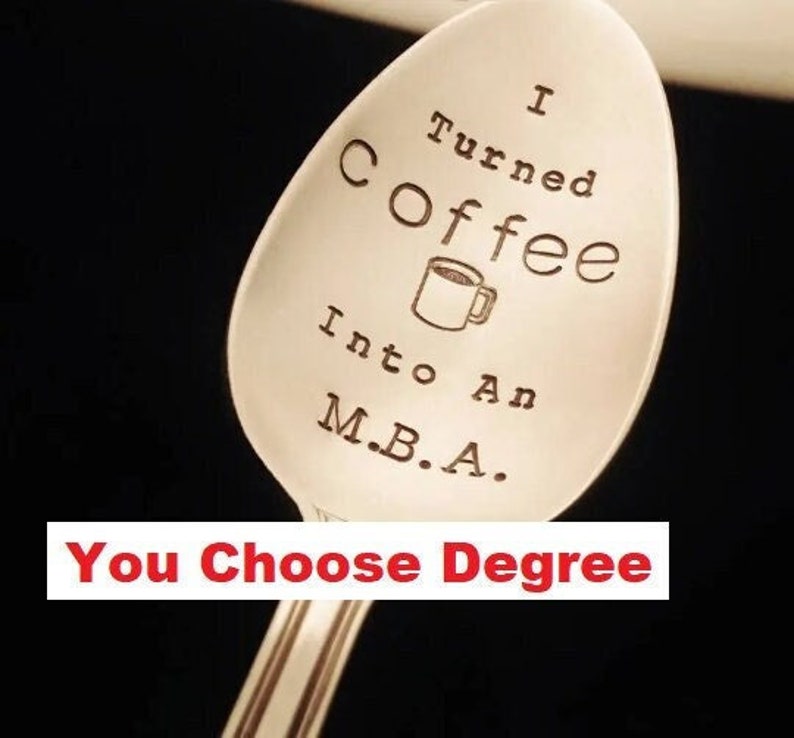 Pu&ograve; includere: Un cucchiaio d'argento con la scritta "I Turned Coffee Into An M.B.A." e un disegno di tazza di caff&egrave;. La frase "You Choose Degree" &egrave; sotto. Il cucchiaio &egrave; su sfondo scuro.