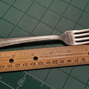 Op de afbeelding: Een zilveren vork met de inscriptie "I FORKING LOVE YOU" op het handvat. De vork is 16,5 cm lang en wordt gemeten tegen een houten liniaal.