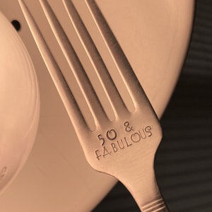 May include: Silver fork with the words "50 & FABULOUS" engraved on the handle.