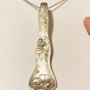 May include: A silver necklace with a pendant made from a vintage spoon. The spoon is engraved with a floral design and has a delicate chain.