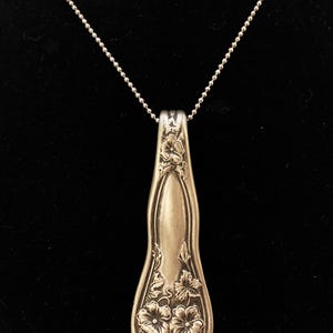 May include: A silver necklace with a pendant made from a vintage spoon. The spoon is decorated with a floral design.