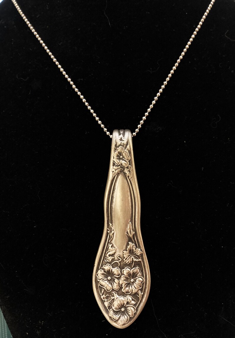 May include: A silver necklace with a pendant made from a vintage spoon. The spoon is decorated with a floral design.