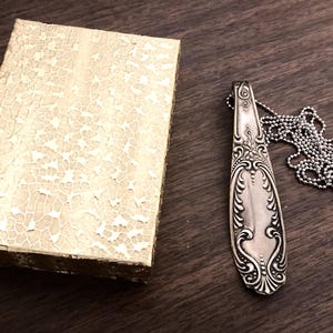 May include: A silver spoon pendant necklace with a decorative design and a silver chain.
