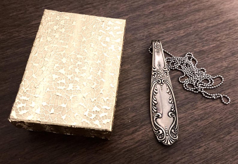 May include: A silver spoon pendant necklace with a decorative design and a silver chain.