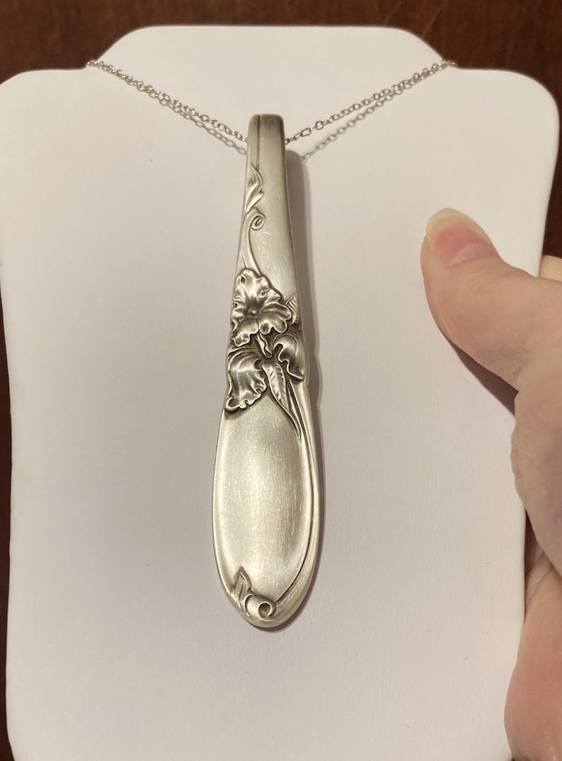Puede incluir: Collar con colgante de plata con dise&ntilde;o en forma de cuchara. El colgante est&aacute; adornado con detalles florales y cuelga de una delicada cadena de plata. El colgante de cuchara mide aproximadamente 15 cm de largo.
