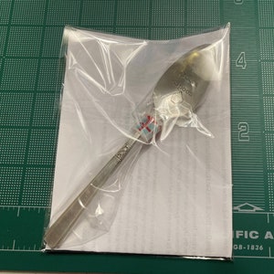 May include: A silver spoon with the words "Hot Cocoa Spoon" engraved on the bowl. The spoon is packaged in a clear plastic bag.