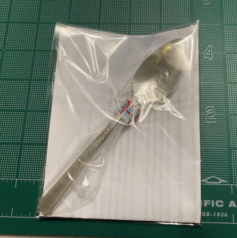 May include: A silver spoon with the words "Hot Cocoa Spoon" engraved on the bowl. The spoon is packaged in a clear plastic bag.