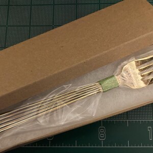 May include: A silver fork with a green ribbon wrapped around the handle is displayed in a brown cardboard box with white tissue paper.