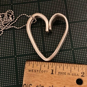 May include: Silver heart-shaped pendant necklace with a delicate chain. The pendant is approximately 1 inch in length.