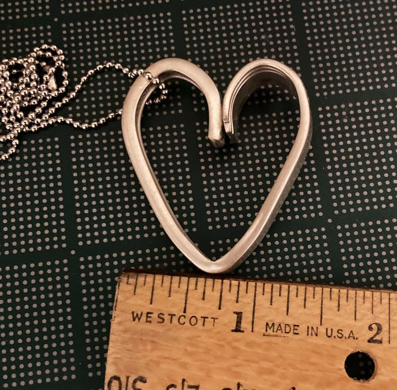 May include: Silver heart-shaped pendant necklace with a delicate chain. The pendant is approximately 1 inch in length.