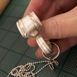 May include: A silver necklace with a chain made of small round beads. The necklace has a pendant made of two silver rings, one with a decorative design.