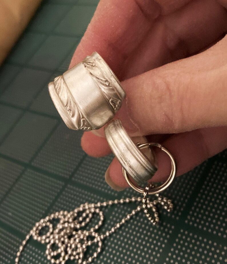 May include: A silver necklace with a chain made of small round beads. The necklace has a pendant made of two silver rings, one with a decorative design.