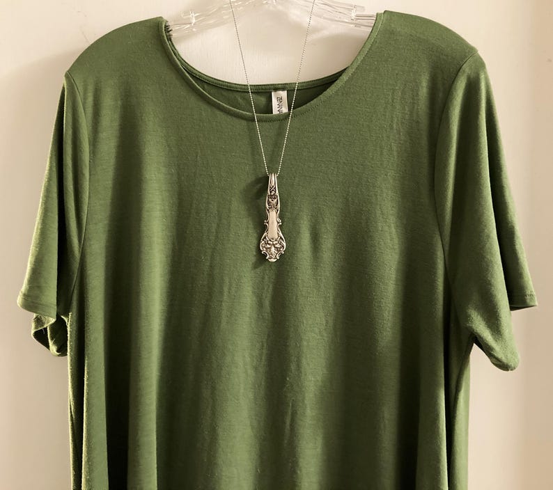 May include: A green t-shirt with a silver spoon pendant necklace.