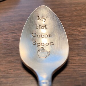 May include: A silver spoon with the words "My Hot Cocoa Spoon" engraved on it. A small illustration of a cup of hot cocoa with whipped cream is also engraved on the spoon.