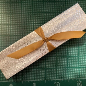 May include: A silver gift box with a gold ribbon tied in a bow. The box has a textured surface.